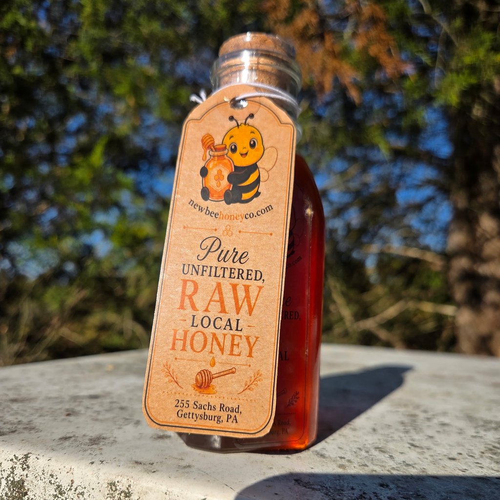 One-pound glass bottle of dark amber raw honey with a cork stopper and a New Bee Honey Co. kraft hang tag